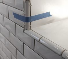 the corner of a white tiled wall with blue tape on it's edge,