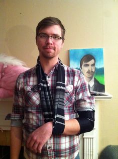 a man with a cast on his arm standing in front of a painting and wearing a plaid shirt