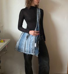 a woman standing in front of a white wall holding a blue bag with stripes on it