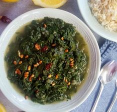 a bowl filled with greens and nuts next to two bowls of rice, lemon wedges and orange slices