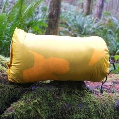 a large yellow pillow sitting on top of a moss covered rock in the middle of a forest