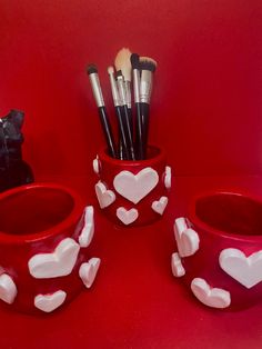 three cups with hearts painted on them and one cup has brushes in the shape of hearts