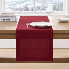 a red table runner with a white plate and fork on it in front of a window