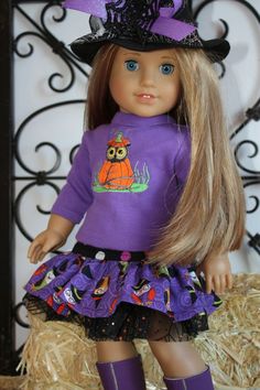 a doll with long hair wearing a purple sweater and black hat, sitting on hay bales