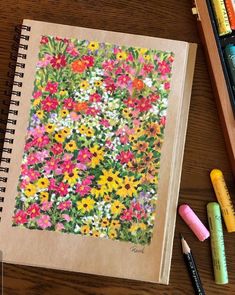 an open notebook with flowers and crayons next to it on a wooden table