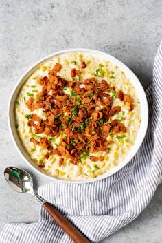 a bowl of mashed potatoes topped with bacon and green onions on a gray surface