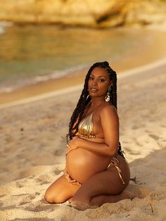 a pregnant woman sitting in the sand at the beach