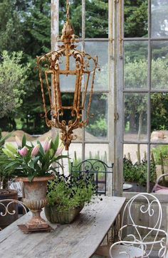 a table with some flowers on it in front of a glass wall and an old chandelier