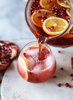 pomegranate being poured into a glass with orange slices on the rims