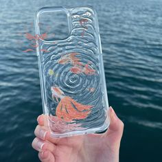 a hand holding up a clear case with fish on it in front of the water