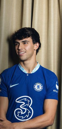 a young man in a blue soccer jersey posing for a photo with his arms crossed