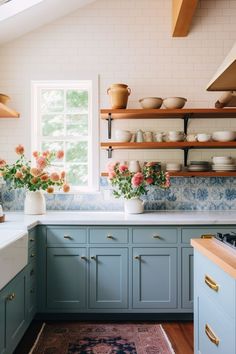 a kitchen with blue cabinets and flowers in vases on the counter top, near a window