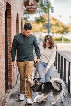 a man and woman are walking their dog down the street with one holding on to his leash