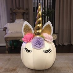 a white pumpkin shaped like a unicorn with pink and purple flowers on its head, sitting on a wooden table