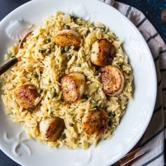 a white plate topped with pasta and scallops on top of a blue table