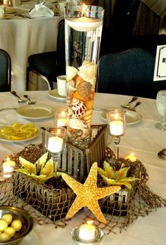 a table topped with plates and candles next to a starfish centerpiece on top of a white table cloth