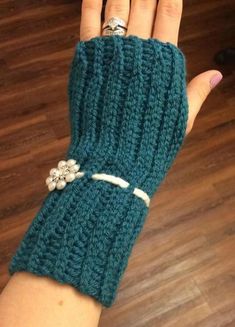 a woman's hand wearing a green knitted glove with flowers on the wrist