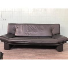 a brown leather couch sitting on top of a hard wood floor next to a white tiled wall