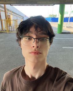 a young man wearing glasses standing in front of a parking lot with his hand on his hip