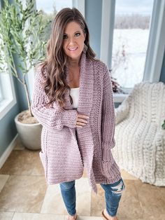 a woman standing in front of a window wearing a pink cardigan sweater and ripped jeans