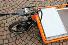 an orange bike with a white board attached to the front wheel and seat on cobblestone pavement