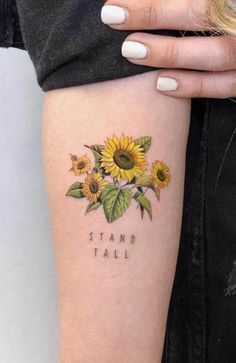 a woman's arm with sunflowers and the words stand tall on it