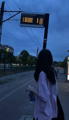 a woman is walking down the street with a water bottle in her hand and an electronic sign above her