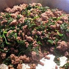 meat and spinach cooking in a pan on the stove