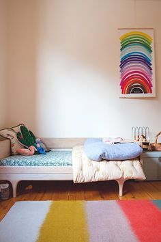 a bedroom with a bed and colorful rugs on the wooden floor, in front of a white wall