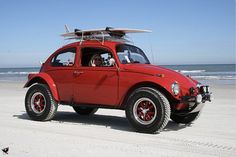 a red car with a surfboard on the roof is parked at the beach in front of the ocean