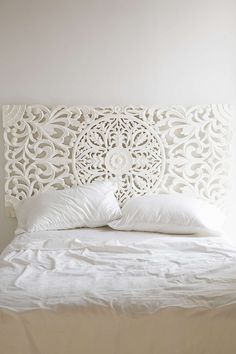 a white bed topped with pillows next to a wall mounted headboard in a bedroom