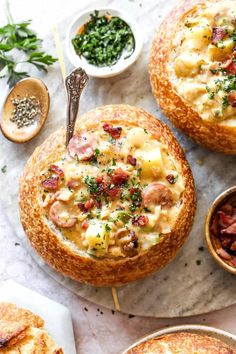 two bread bowls filled with food on top of a marble counter next to other dishes