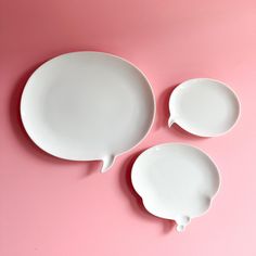 three empty white plates with speech bubbles on them against a pink background, top view