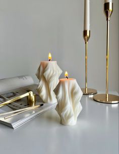 two candles sitting on top of a table next to a magazine and candle holders with books