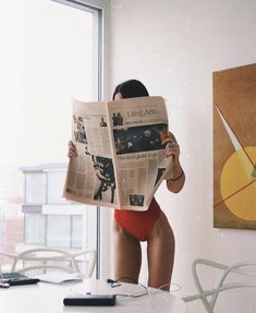 a woman in a red swimsuit is reading a newspaper while sitting at a table