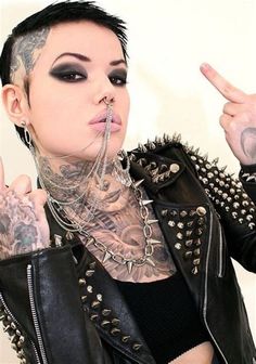 a woman with tattoos and piercings on her head pointing to the side while wearing a black leather jacket