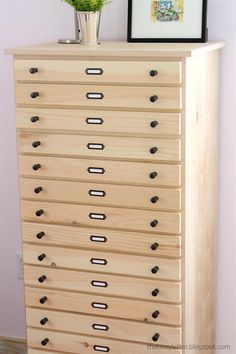 a wooden dresser with many drawers and a flower vase on top of it, against a wall