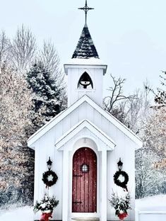 a small church with wreaths on the front door and steeple is covered in snow