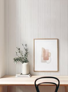 a desk with a chair, vase and plant on it in front of a striped wall