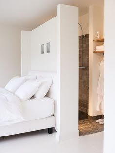 a bed with white sheets and pillows in a room next to a shower stall on the wall