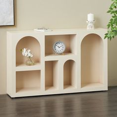 a white shelf with three shelves and a clock on it next to a potted plant