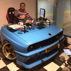 a man sitting in front of a blue car with electronic equipment on it's hood