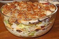 a large hamburger in a glass bowl on top of a wooden table with other food items