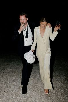 a man and woman dressed in formal wear walking down the street at night with drinks