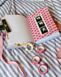 an open book sitting on top of a bed next to some pink and white tape