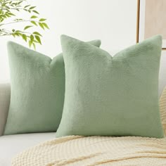 two green pillows sitting on top of a white couch next to a potted plant