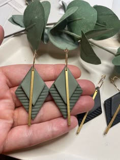 a pair of earrings is being held in someone's hand next to some plants