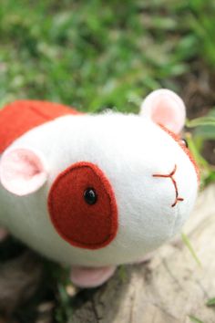 a white and red stuffed animal sitting on top of a grass covered ground next to a tree