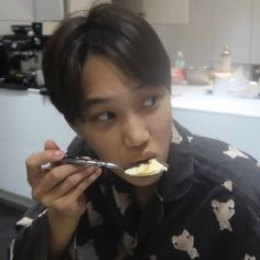 a young man eating food with a spoon in his mouth and looking at the camera