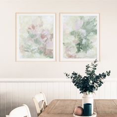 two paintings hanging on the wall above a wooden table with chairs and vase filled with flowers